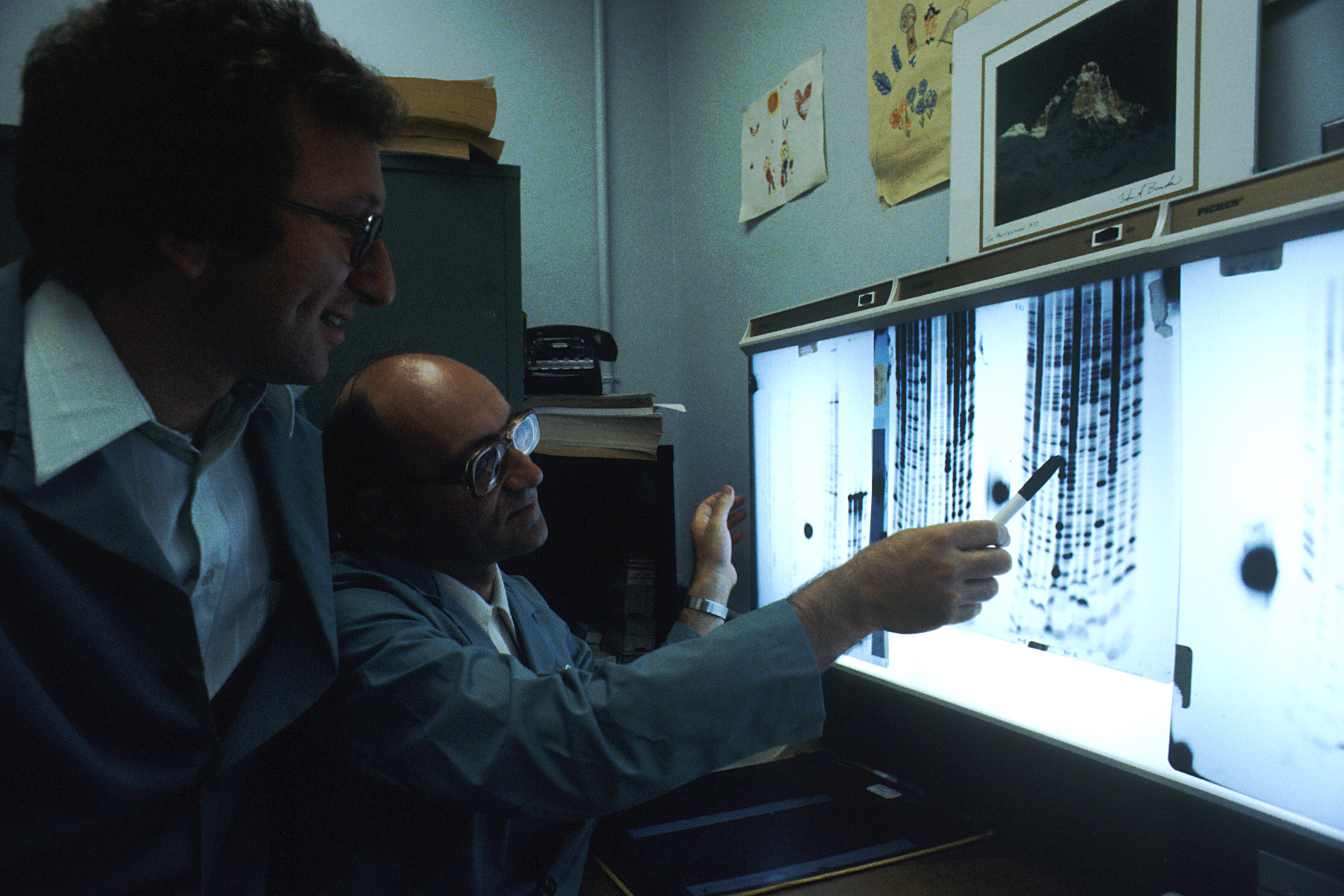 Dos científicos revisan una visualización de secuenciación de ADN en un laboratorio, imagen asociada a estudios genéticos.
