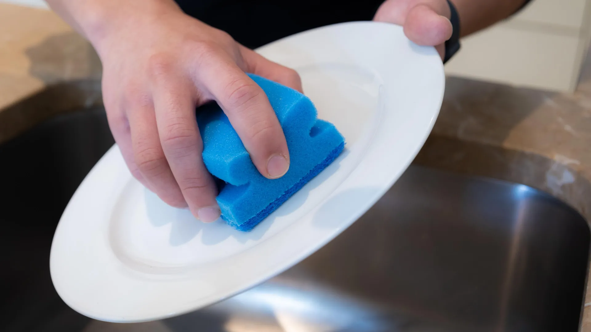 Esponja azul con espuma durante el lavado manual de platos