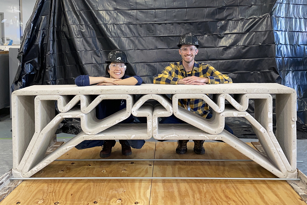 Investigadores del MIT posan detrás de un pequeño puente de concreto impreso en 3D durante una prueba de carga