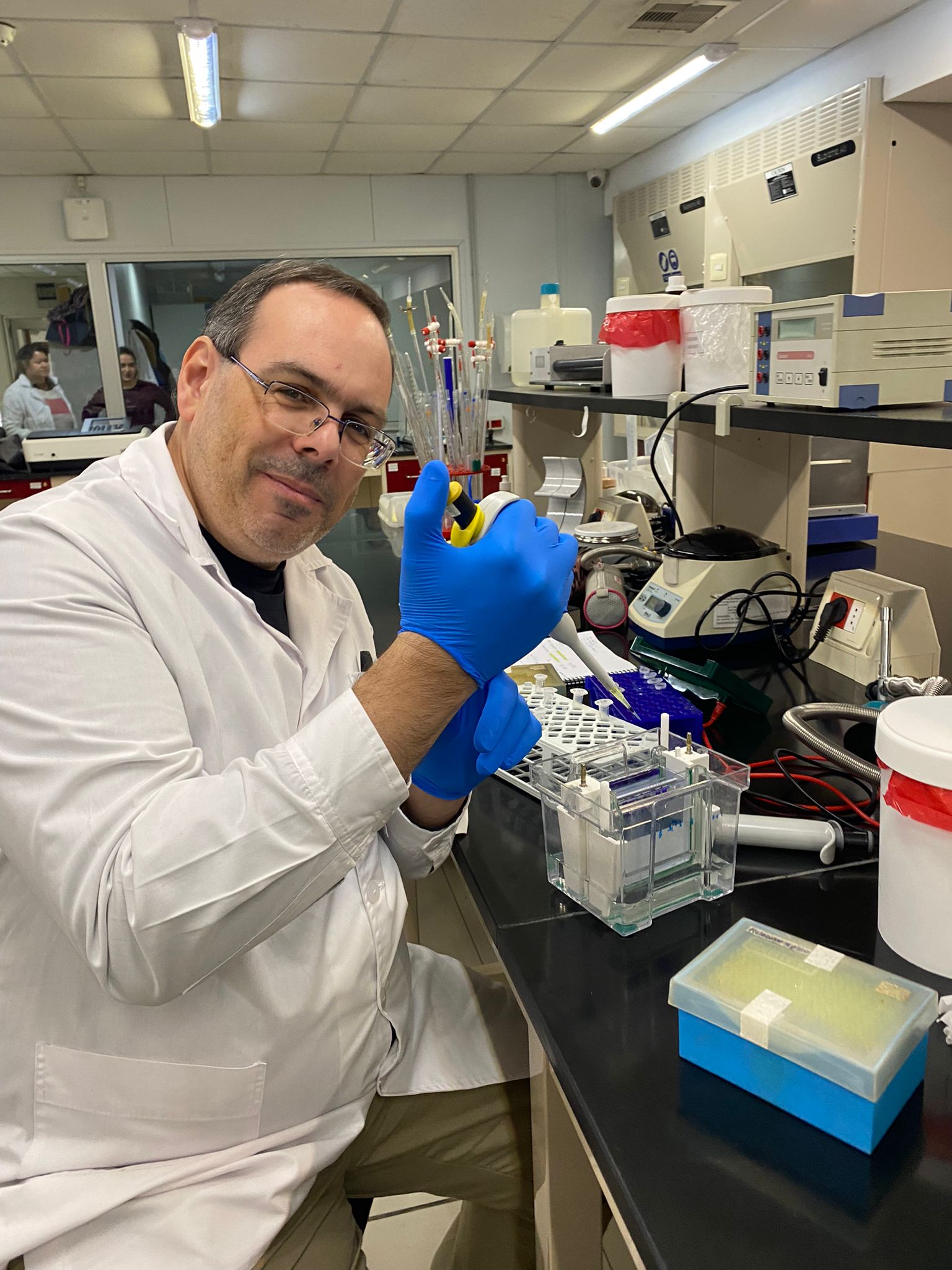 Federico de los Santos en un laboratorio, con túnica blanca y guantes, trabajando con instrumental científico.